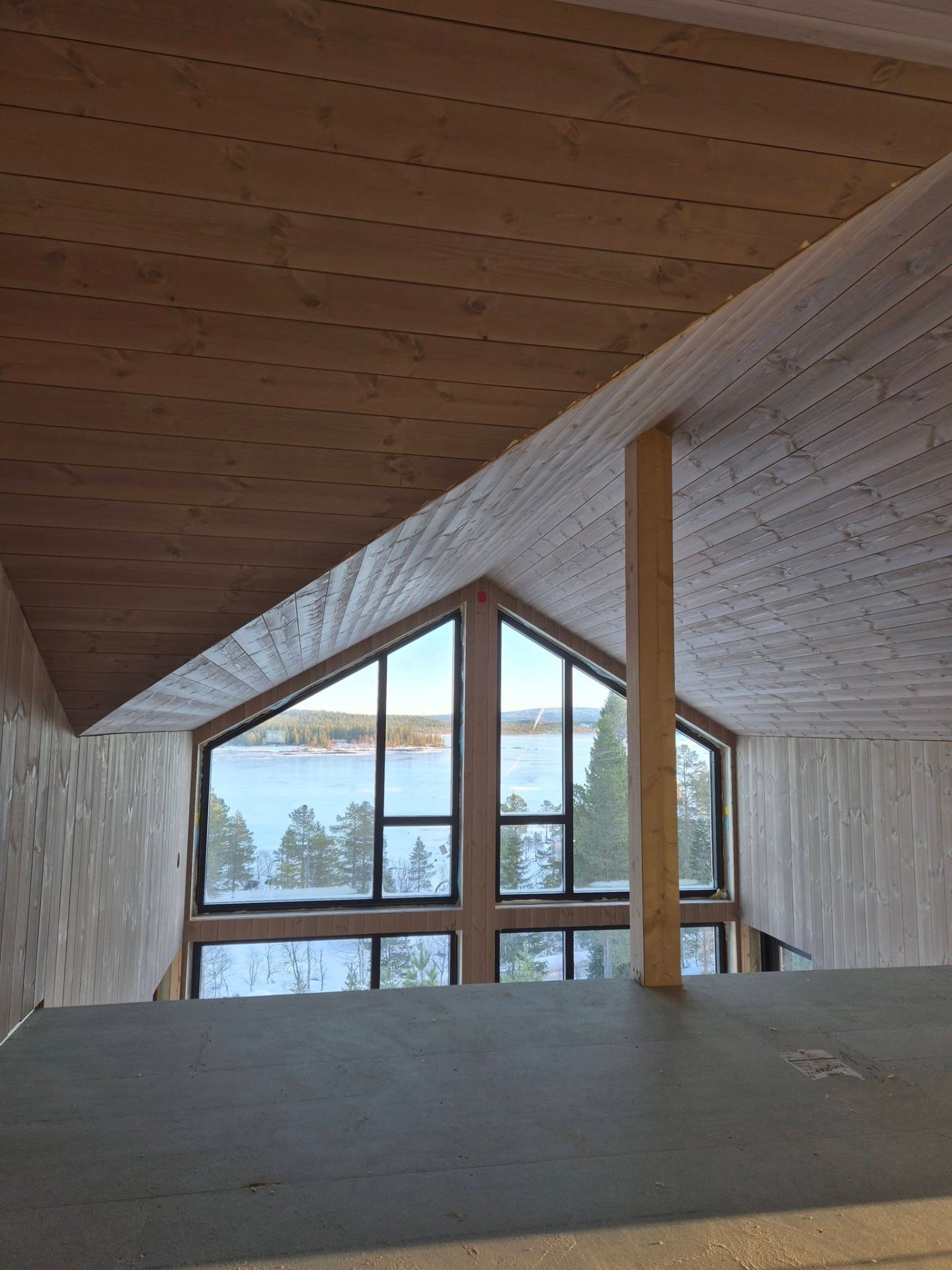 Hyttestue med lys panel og stort panoramavindu mot vann og fjell – interiør av Byggservice 1 AS