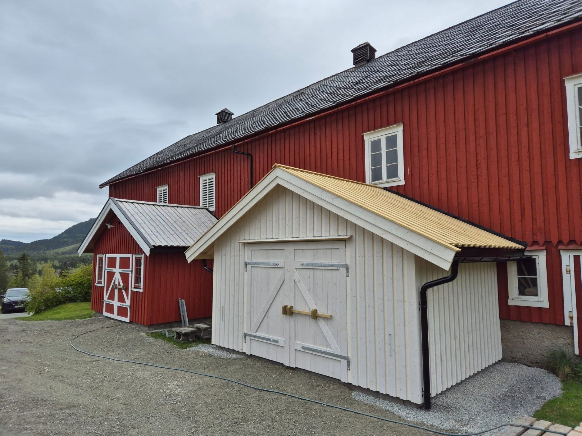Nytt hvitt uthus i tre inntil rød låve – nybygg av Byggservice 1 AS